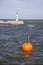 Orange buoy and lighthouse in sea dock