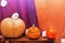 orange candles and Halloween pumpkin on textured surface in front of violet backdrop