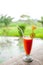 Orange and carrot juice in glass with mint, fresh vegetables and fruits on wooden table in outdoor terrace on greenery background