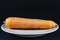 Orange carrot on a plate isolated on a black background in a studio shot, unpeeled, a single carrot, ready to be prepared