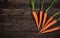 Orange carrot roots with green leaves on dark wooden board, photo from above, space for text left side