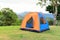 Orange color family camping tent with ground sheet setup on green park campsite