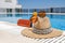 Orange colored beach accessories near swimming pool. Sun cream, sunglasses, music speaker and straw hat