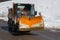 Orange-coloured Snowplough Operating on the Road with Snow on the Edges