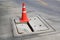 Orange cone warning for cracked concrete drain cover on the cement road