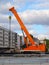 Orange crawler crane at the site of road construction works in the city against the background of a residential building and the s