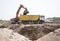 orange crawler excavator pours earth into body of yellow dump truck