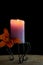 Orange daylily and burning purple candle against black background