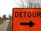 Orange detour sign with black arrow with trail or path