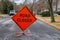 Orange diamond shaped road closure sign on road in a neighborhood near a house.