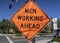 Orange diamond shaped traffic control sign reading â€œMen Working Aheadâ€