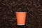 Orange disposable cup of coffee to go on the background of roasted beans