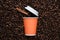 Orange disposable cup of coffee to go with a cinnamon stick on the background of roasted beans