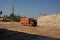 An orange dump truck, lorry full of stones in a sand quarry, transporting of materials on a natural background.