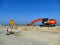 Orange excavator on pile of sand with road signs on construction