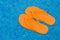 Orange flip flops floating in blue pool water