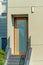 Orange framed wood door made with glass or acrylic on grey stairs with hand rails and a beige stucco house.