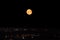 Orange full moon on night sky above city lights