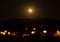 Orange full moon rising over the village mountain.