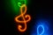 Orange glowing neon treble clef on black background.