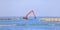 Orange grab excavator lays stones in the sea, making a breakwater