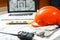 Orange hard hat, laptop  with drawings, level meter, walkie talkie and gloves lying on a  blueprints on a table