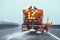 Orange highway maintenance gritter truck spreading de-icing salt on road in winter