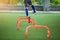 Orange hurdles markers on green artificial turf with blurry kid soccer is jumping cross it