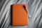 Orange journal notebook with pen on bed.