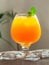 Orange juice in a brandy glass with a sprig of mint. On a wooden background. Next to a glass of ice cubes. Light background. Close