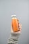 Orange juice in glass bottle on women hands with sweater on light gray background. vertical image