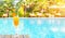 Orange juice glass on wooden table with swimming pool view background