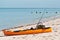 Orange kayak, fitted for fishing, resting on sandy, tropical beach