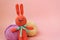 Orange knitted hare stands on the background of multi-colored balls of yarn on a pink background. There is a place for text