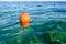 Orange large round plastic air-inflated life-saving beacon, buoy floats in the blue salt sea for safety.