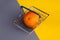 Orange lies in a shopping basket on gray and yellow backgrounds