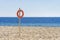 Orange lifebuoy in empty sandy beach in front of Mediterranean sea. Life saving lifeguard buoy, lifebelt on the pole