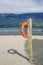 An orange lifebuoy hanging on a wooden pole on a beach near a lake shore