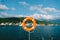 Orange lifebuoy on a metal stand against the backdrop of mountains, water and sky.