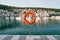 Orange lifebuoy on a stand on a pier against the backdrop of a colorful resort town with moored yachts