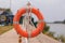 The orange lifebuoy is tied to a fence on the river pier. frontal view