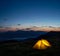 Orange lighted tent in mountains under evening sky