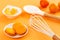 Orange macarons or macaroons in a white saucer with tangerine peeled segments, white whisk and spoon over orange background