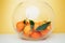 Orange mandarins clementine with green leaves in round clear vase on a white-yellow background