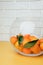 Orange mandarins clementine with green leaves in round clear vase on a white-yellow background