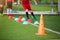 Orange marker cones on green artificial turf with blurry kid soccer player jogging between marker cones for training