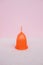 Orange menstrual cup on a pink background.