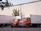 Orange middle semi trucks with box trailers stand in warehouse d