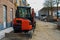 Orange mini excavator on a residential street. Cable drums  equipment container  worker on the background.