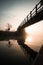 Orange misty foggy sunrise from from under wooden bridge over river reflected in canal. Beautiful reflection in still tranquil.